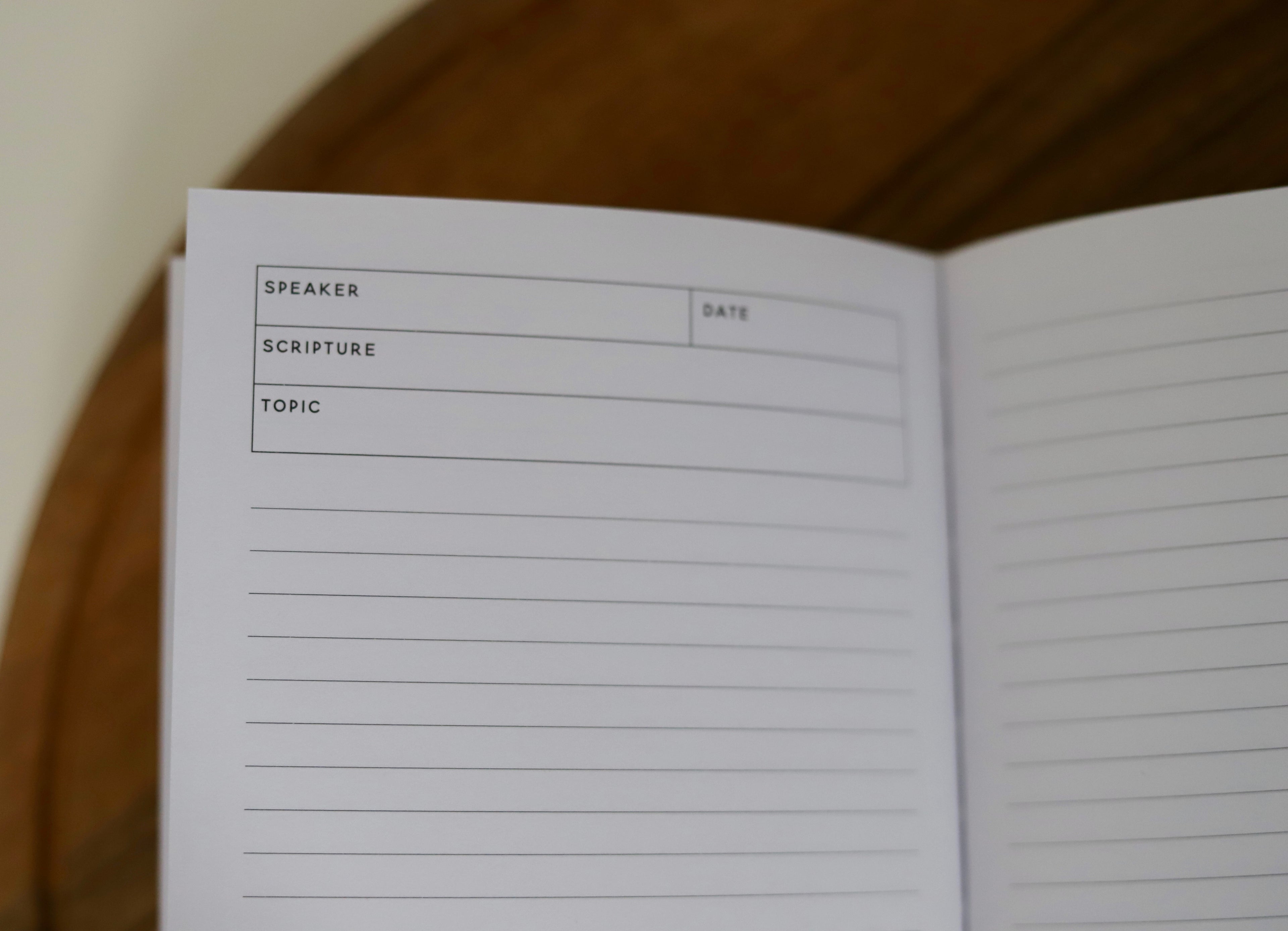 Open notebook with a page titled 'Speaker', 'Scripture', and 'Topic' on a wooden surface.